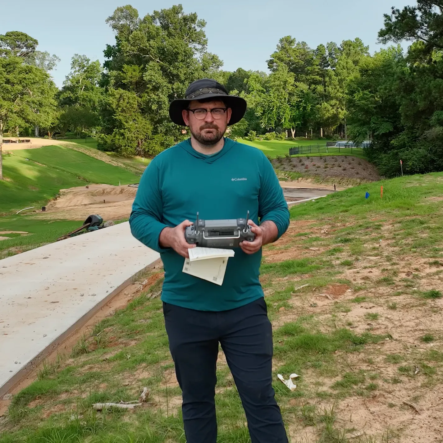 Jacob Caudell on a golf course under construction, holding a drone controller and field notes.
