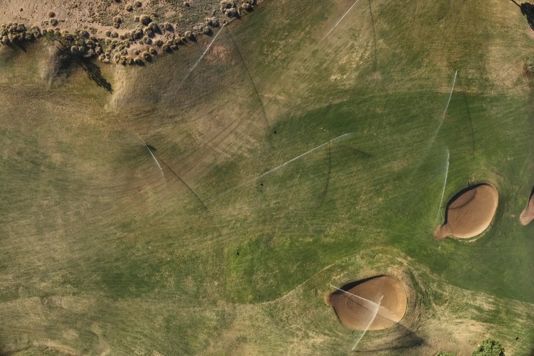 Aerial view of the Links Course at Odessa Country Club with irrigation heads firing across the fairway and over a bunker.